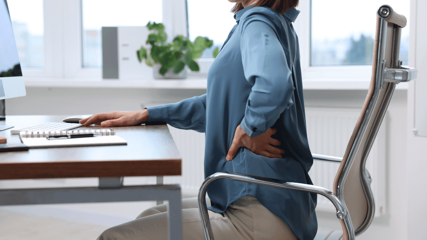 Woman at a desk holding her lower back